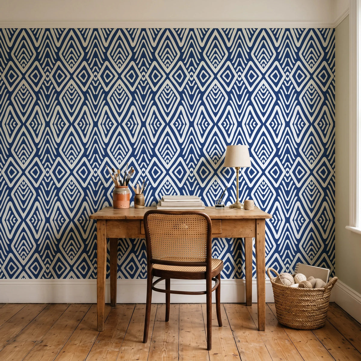Aztec Quilt Indigo geometric tribal wallpaper behind a vintage writing desk in a cozy craft-room home office
