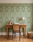 Aztec Quilt Olive geometric tribal wallpaper behind a vintage writing desk in a cozy craft-room home office