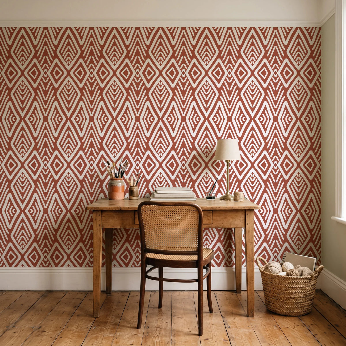 Aztec Quilt Terracotta geometric tribal wallpaper behind a vintage writing desk in a cozy craft-room home office