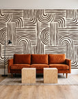 Bantu Lines Espresso brush geometric wallpaper behind a rust velvet sofa in a bright coworking lounge