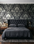 Blushed Whisper Graphite distressed damask wallpaper behind a tufted headboard in a dark, moody bedroom