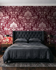 Blushed Whisper Oxblood distressed damask wallpaper behind a tufted headboard in a dark, moody bedroom