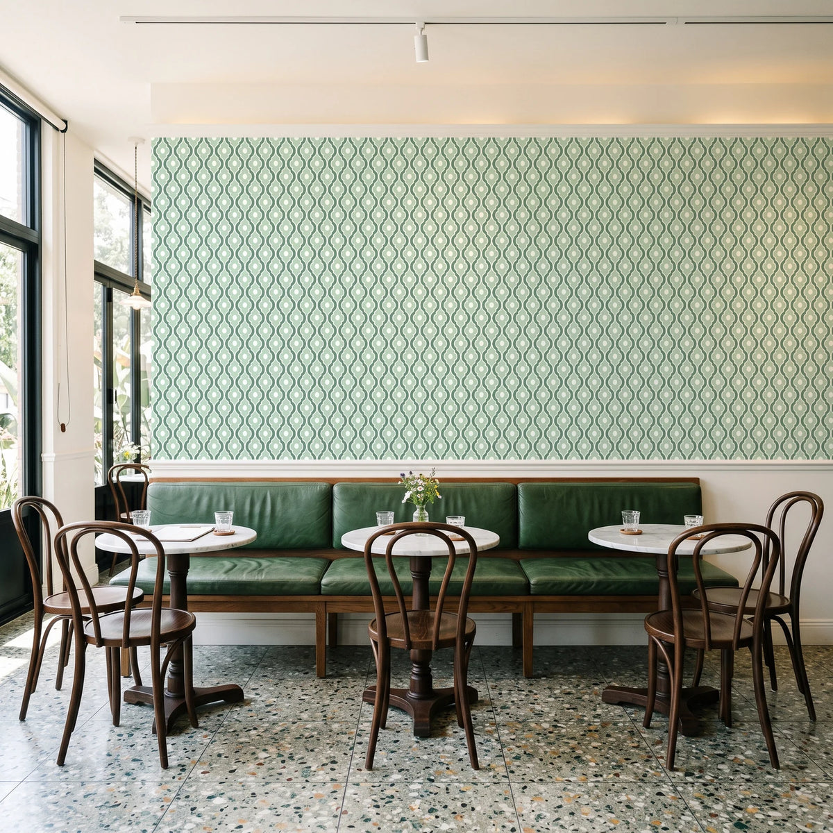 Butter Ogee Sage ogee trellis wallpaper above a green leather banquette in a sunlit neighborhood cafe