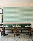 Butter Ogee Sage ogee trellis wallpaper above a green leather banquette in a sunlit neighborhood cafe