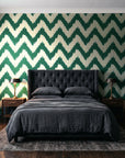 Caramel Drip Emerald chevron wallpaper behind a tufted headboard in a dark, moody bedroom