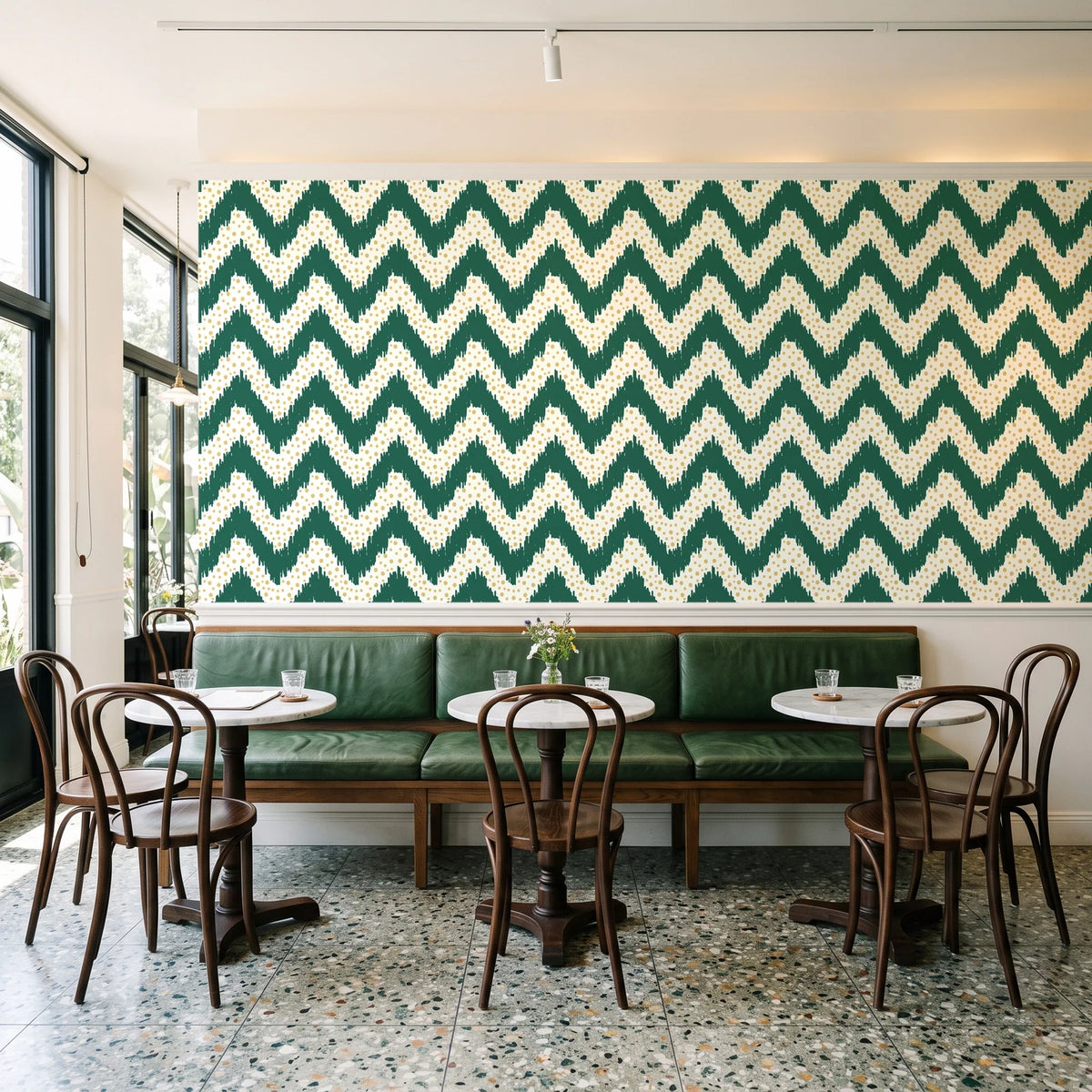 Caramel Drip Emerald chevron wallpaper above a green leather banquette in a sunlit neighborhood cafe