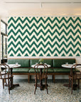 Caramel Drip Emerald chevron wallpaper above a green leather banquette in a sunlit neighborhood cafe