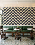 Caramel Drip Midnight chevron wallpaper above a green leather banquette in a sunlit neighborhood cafe