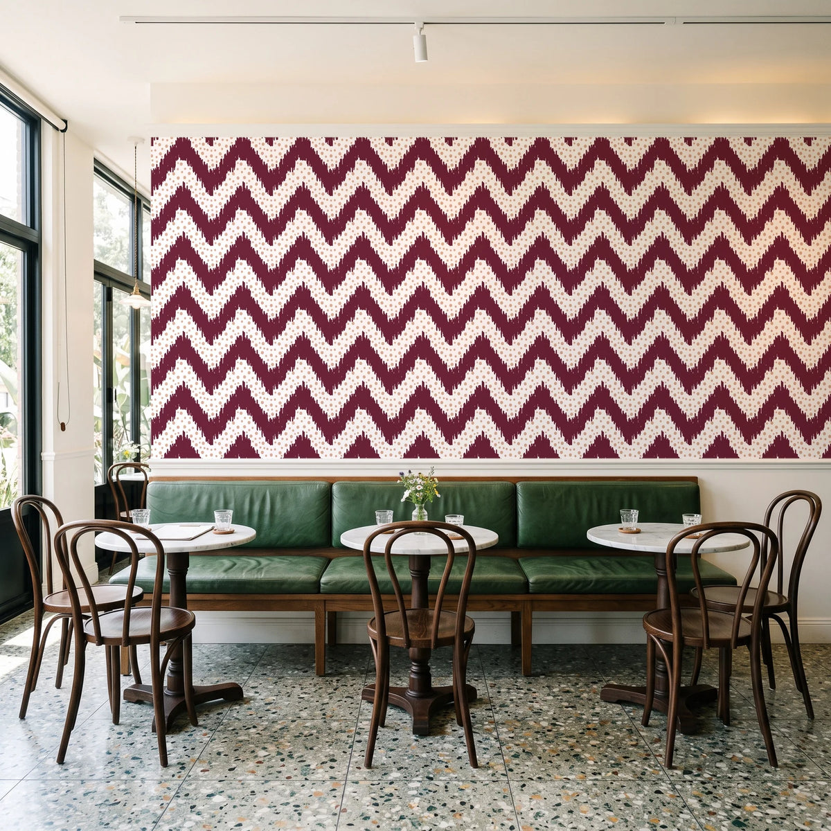 Caramel Drip Oxblood chevron wallpaper above a green leather banquette in a sunlit neighborhood cafe