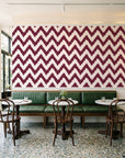 Caramel Drip Oxblood chevron wallpaper above a green leather banquette in a sunlit neighborhood cafe