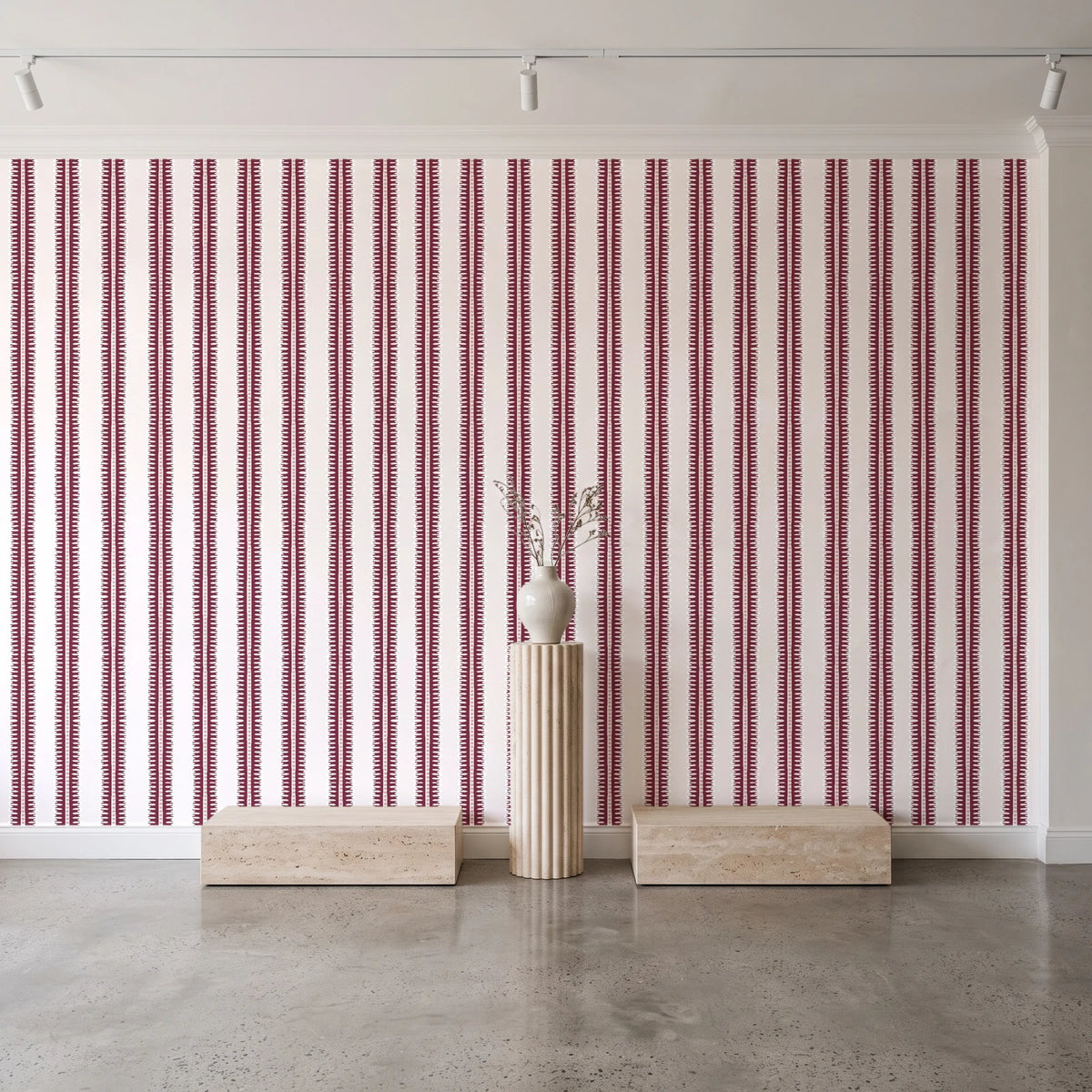 Citrine Column Oxblood stripe wallpaper behind a travertine pedestal and vase in a minimal boutique