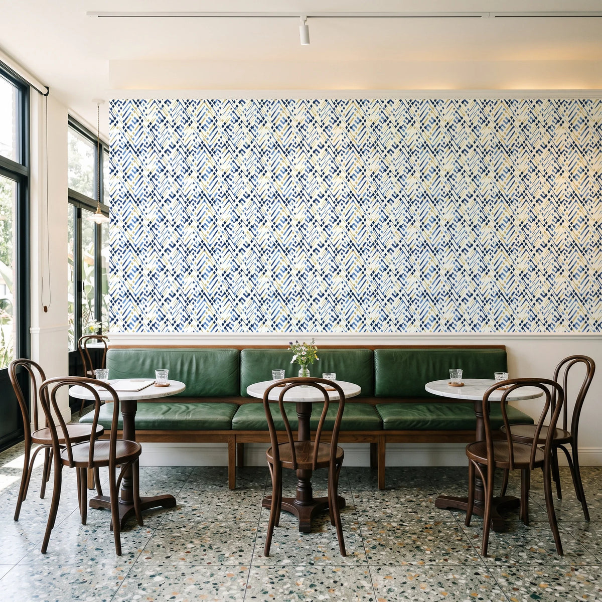 Crossroads Indigo geometric wallpaper above a green leather banquette in a sunlit neighborhood cafe