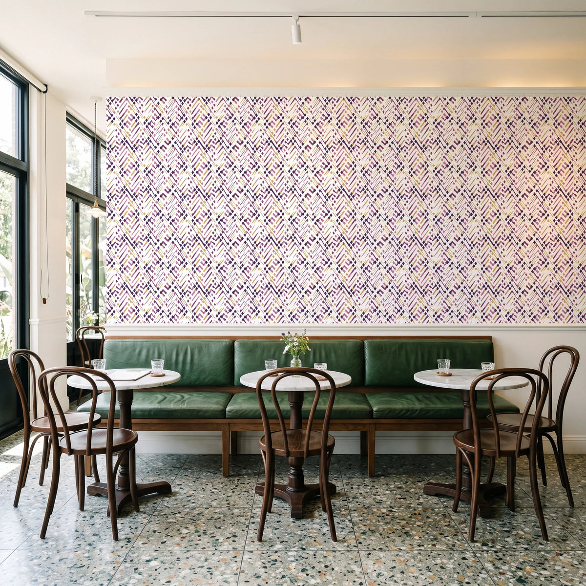 Crossroads Plum geometric wallpaper above a green leather banquette in a sunlit neighborhood cafe
