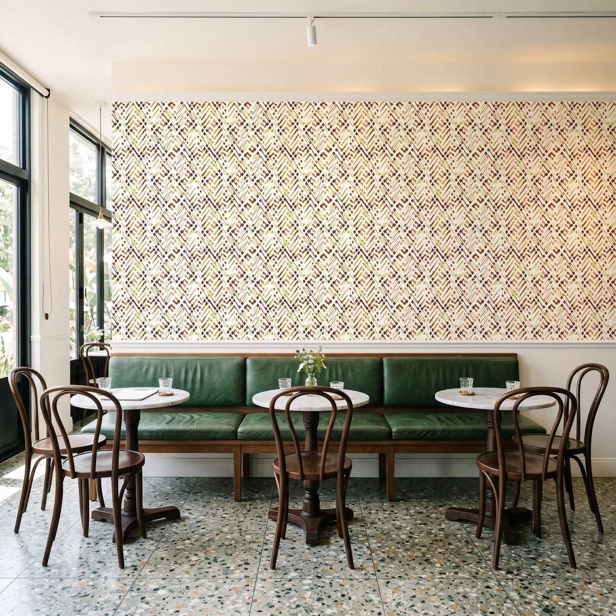 Crossroads Terracotta geometric wallpaper above a green leather banquette in a sunlit neighborhood cafe