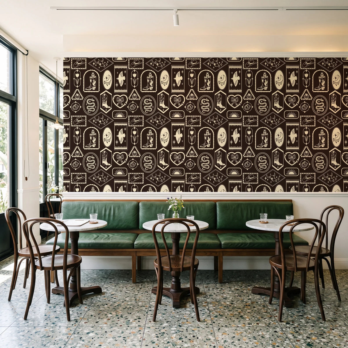 Desert Charms Espresso western icon wallpaper above a green leather banquette in a sunlit neighborhood cafe
