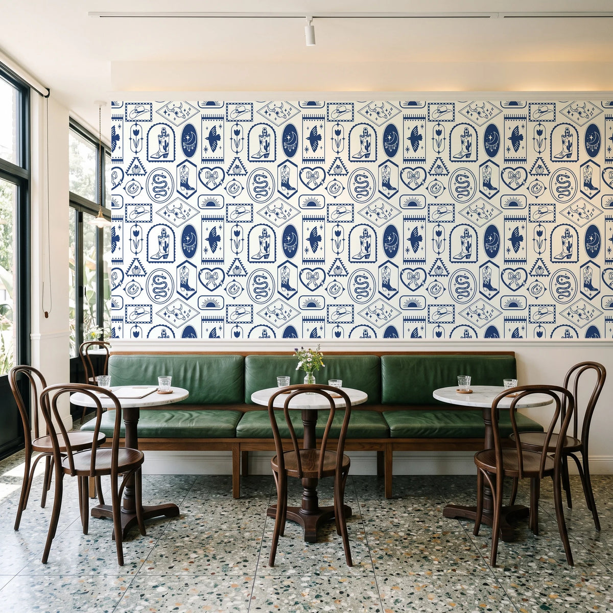 Desert Charms Indigo western icon wallpaper above a green leather banquette in a sunlit neighborhood cafe