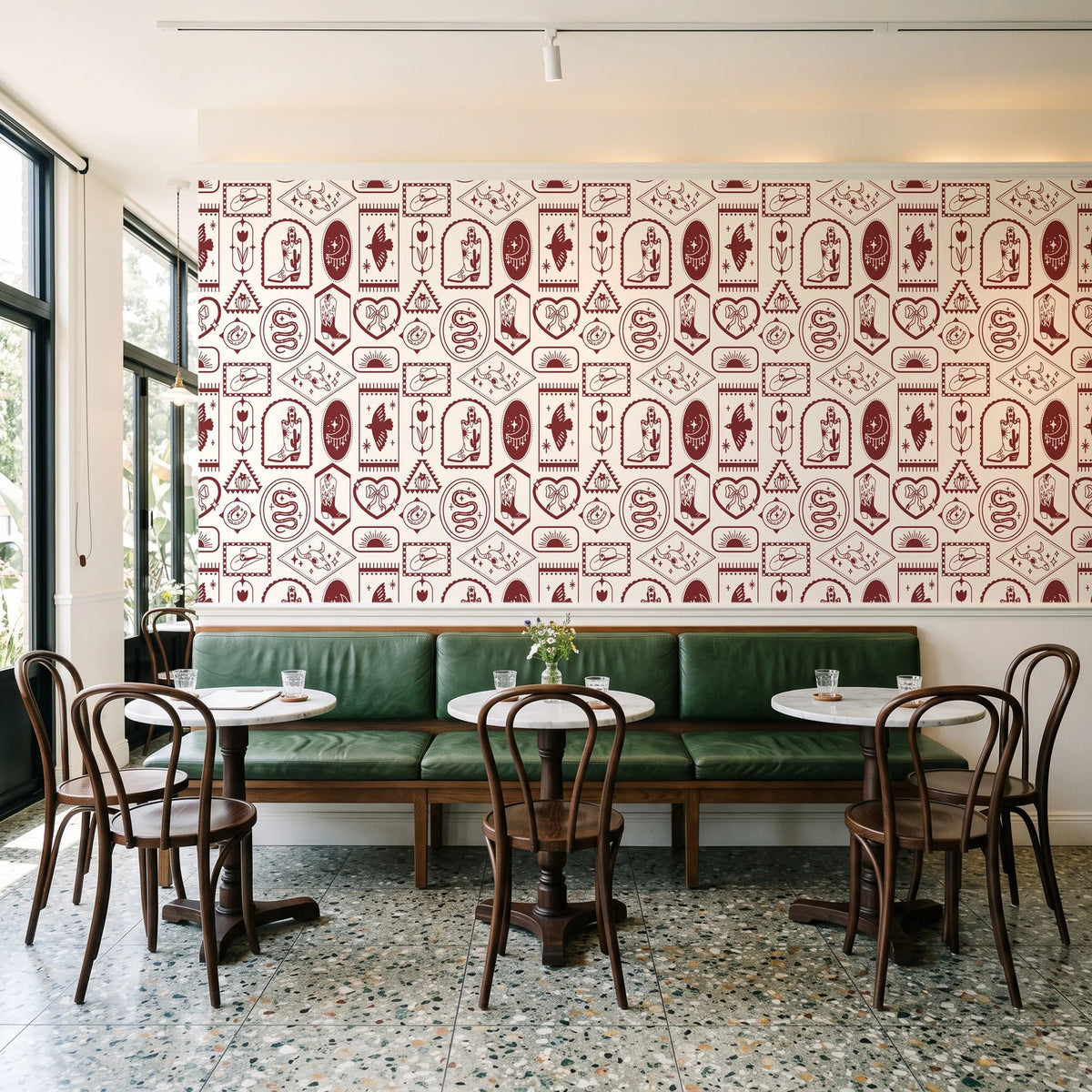 Desert Charms Oxblood western icon wallpaper above a green leather banquette in a sunlit neighborhood cafe