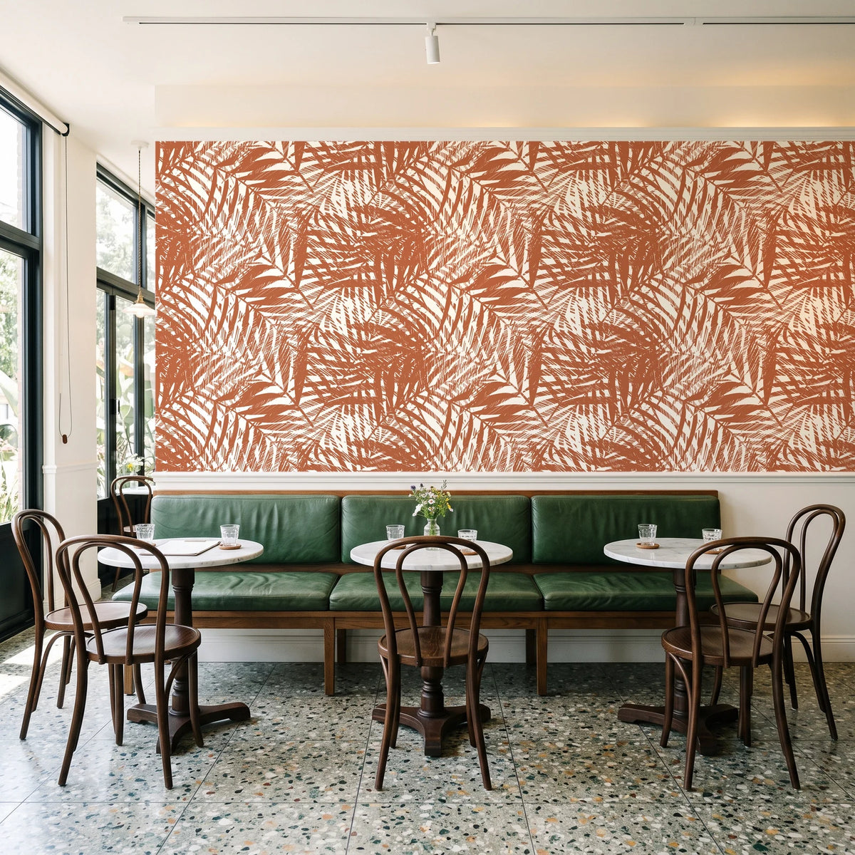 Desert Frond Clay palm frond wallpaper above a green leather banquette in a sunlit neighborhood cafe