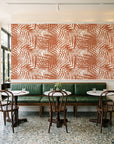Desert Frond Clay palm frond wallpaper above a green leather banquette in a sunlit neighborhood cafe