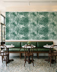 Desert Frond Emerald palm frond wallpaper above a green leather banquette in a sunlit neighborhood cafe