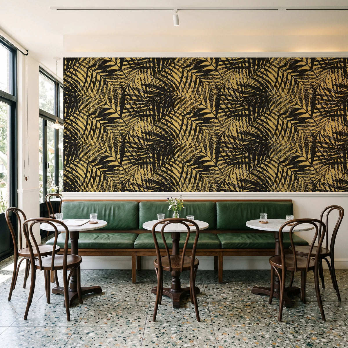 Desert Frond Gilt palm frond wallpaper above a green leather banquette in a sunlit neighborhood cafe