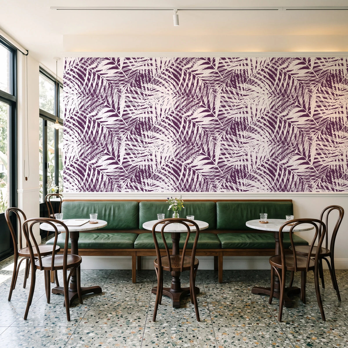 Desert Frond Plum palm frond wallpaper above a green leather banquette in a sunlit neighborhood cafe