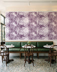Desert Frond Plum palm frond wallpaper above a green leather banquette in a sunlit neighborhood cafe