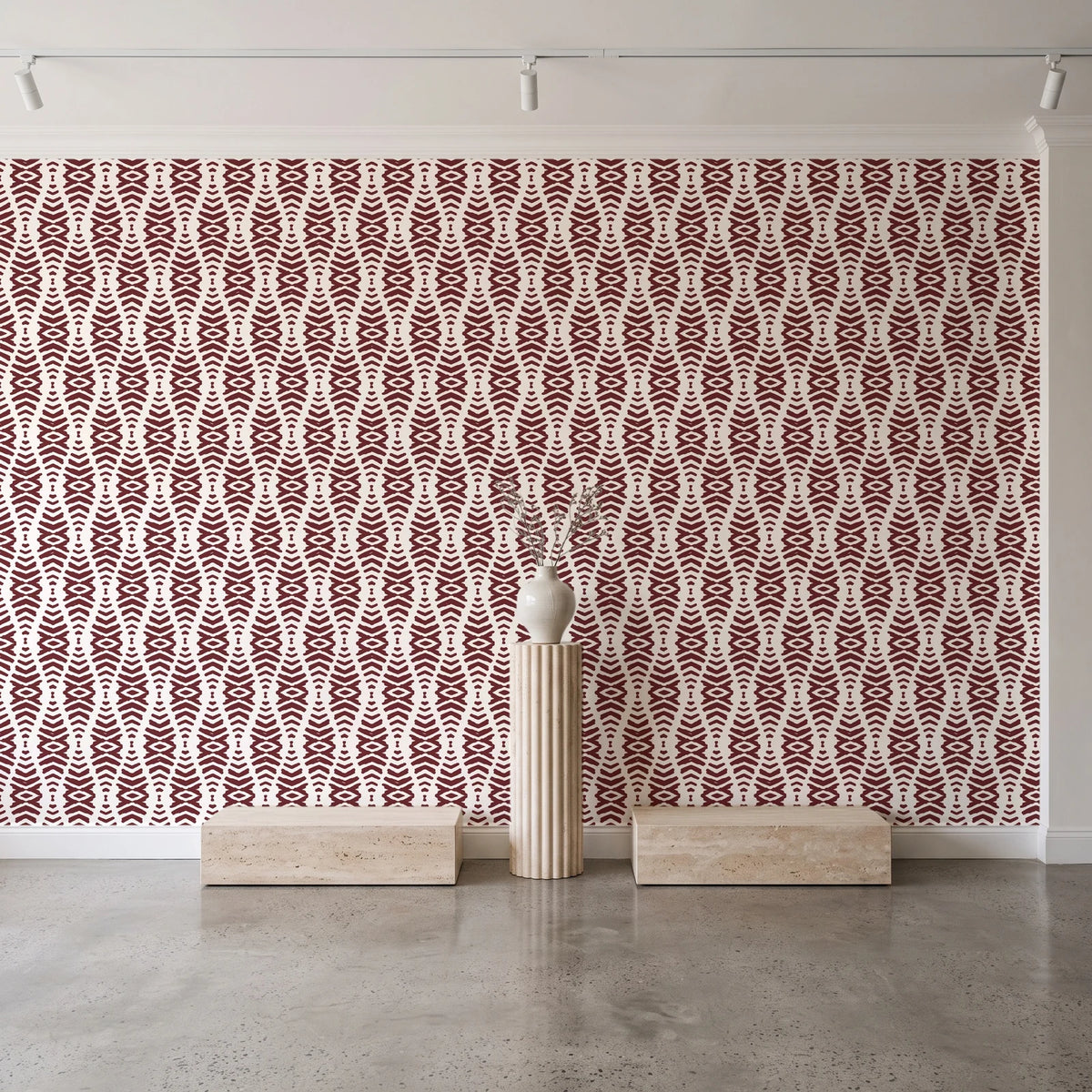 Desert Ritual Oxblood tribal geometric wallpaper behind a travertine pedestal and vase in a minimal boutique