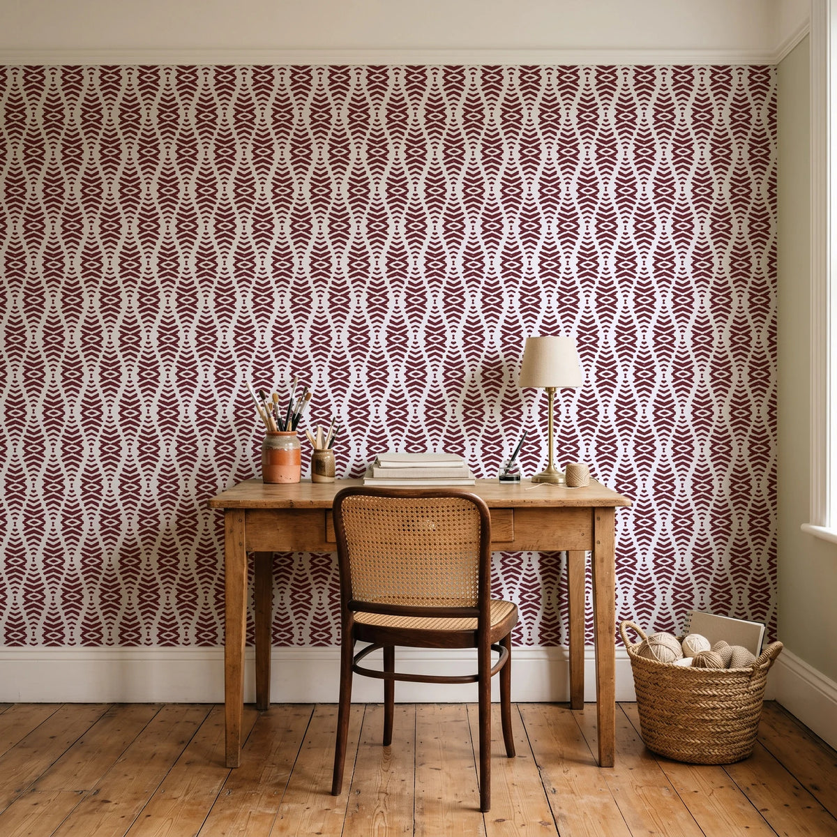 Desert Ritual Oxblood tribal geometric wallpaper behind a vintage writing desk in a cozy craft-room home office