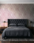Diamond Echo Bordeaux tribal diamond wallpaper behind a tufted headboard in a dark, moody bedroom