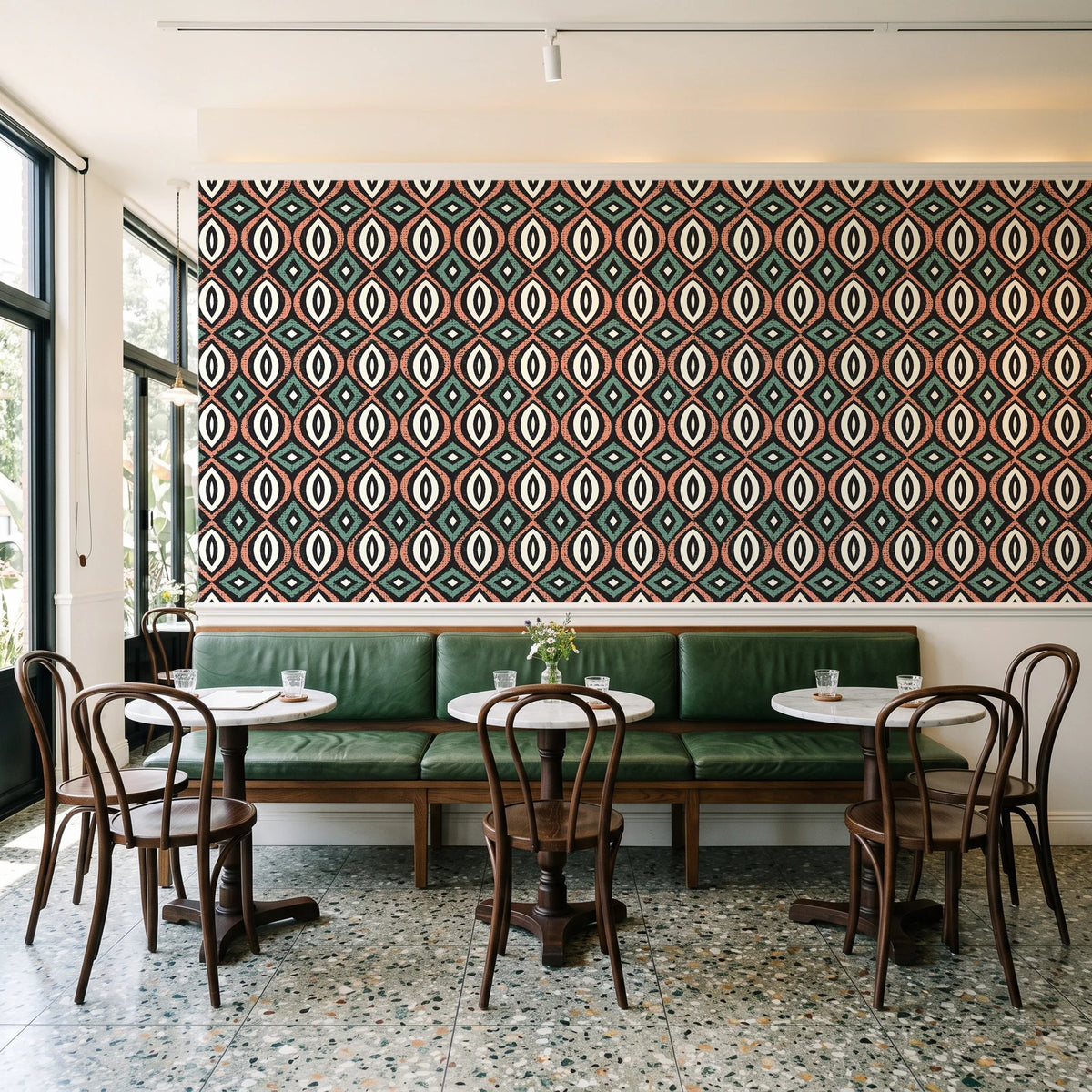 Ember & Iron Forest retro ogee wallpaper above a green leather banquette in a sunlit neighborhood cafe