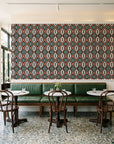 Ember & Iron Forest retro ogee wallpaper above a green leather banquette in a sunlit neighborhood cafe