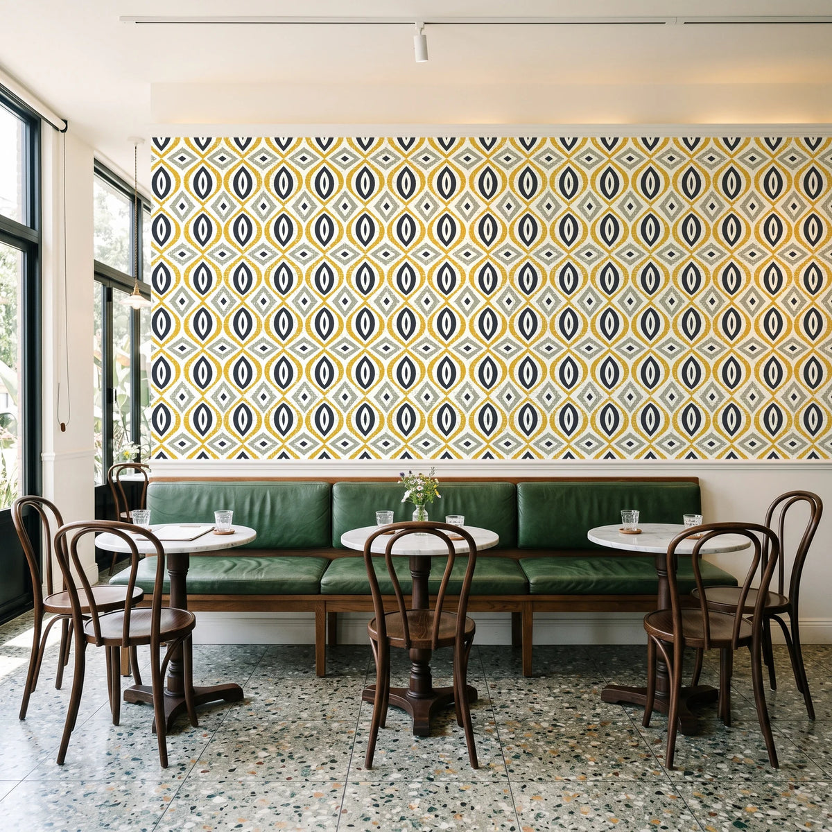 Ember & Iron Mustard retro ogee wallpaper above a green leather banquette in a sunlit neighborhood cafe