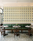 Ember & Iron Mustard retro ogee wallpaper above a green leather banquette in a sunlit neighborhood cafe