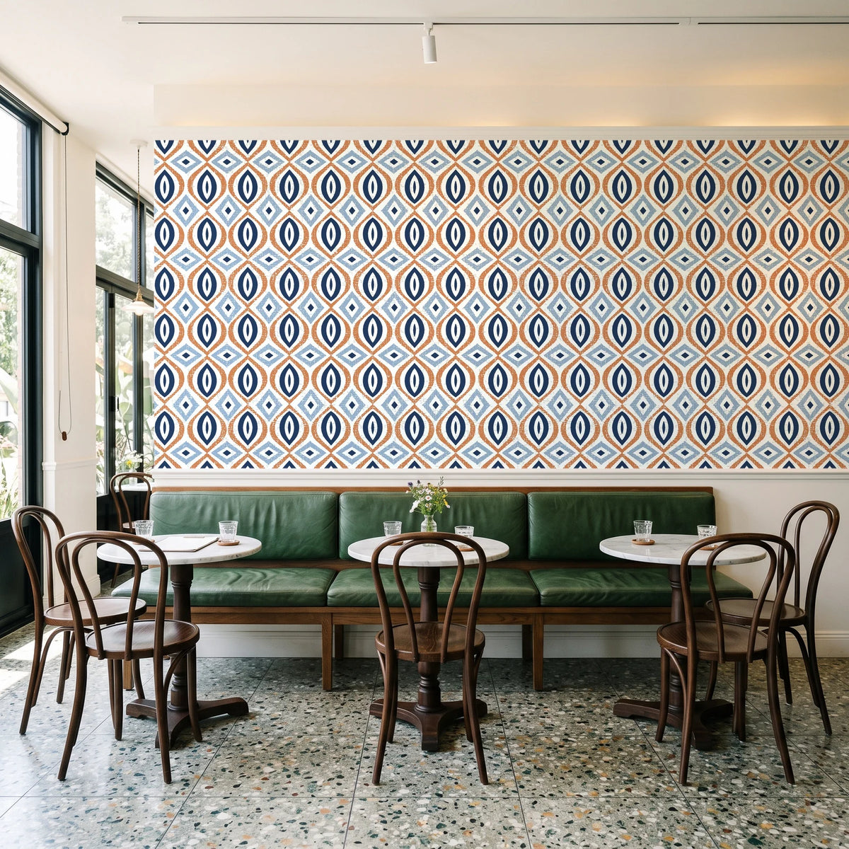 Ember & Iron Navy retro ogee wallpaper above a green leather banquette in a sunlit neighborhood cafe