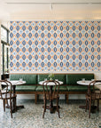 Ember & Iron Navy retro ogee wallpaper above a green leather banquette in a sunlit neighborhood cafe