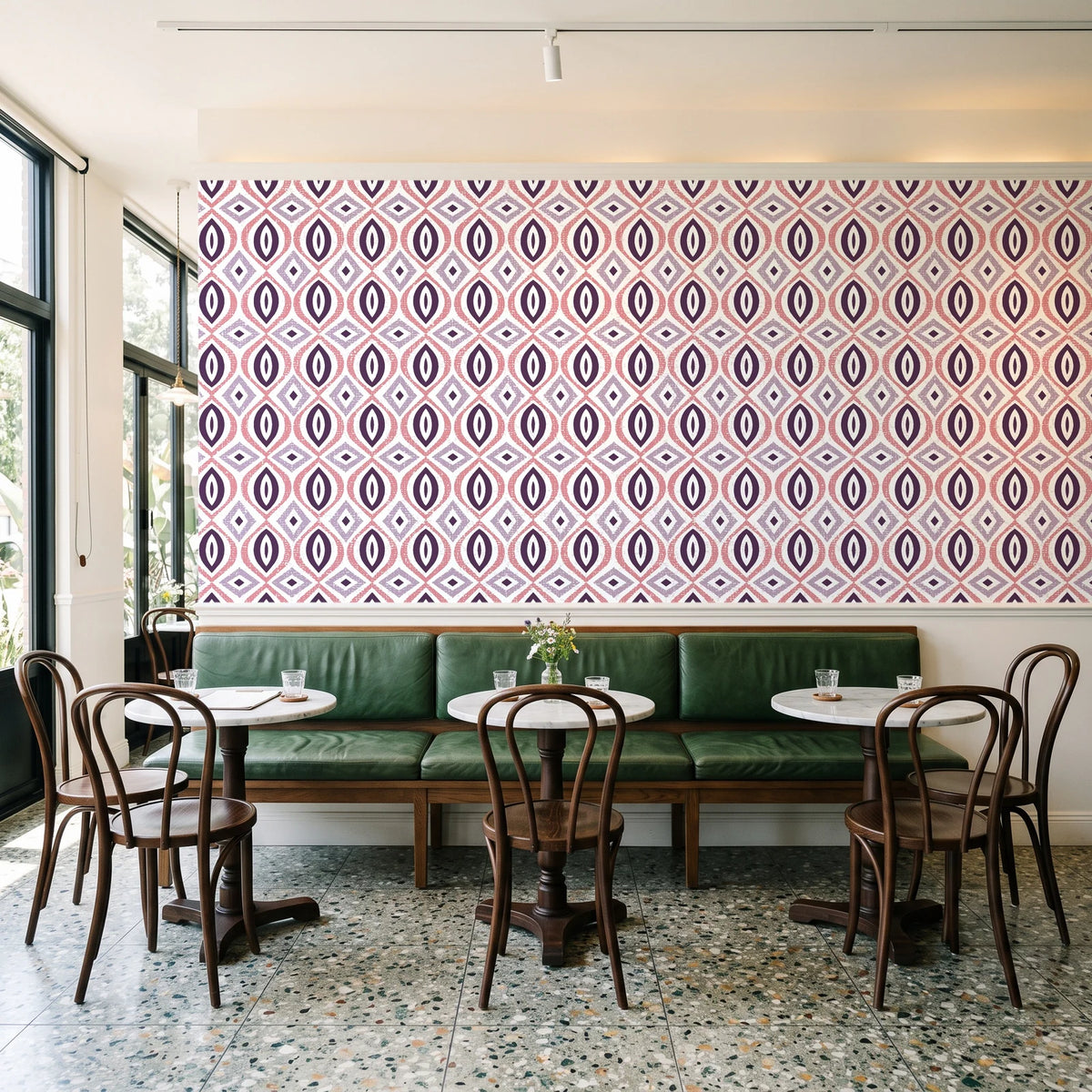 Ember & Iron Plum retro ogee wallpaper above a green leather banquette in a sunlit neighborhood cafe