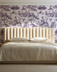 Garden Folly Plum pastoral toile wallpaper behind a channel-tufted bed in a calm primary bedroom