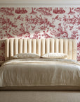 Garden Folly Rouge pastoral toile wallpaper behind a channel-tufted bed in a calm primary bedroom