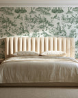 Garden Folly Sage pastoral toile wallpaper behind a channel-tufted bed in a calm primary bedroom