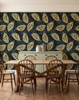 Gilded Frond Noir leaf wallpaper in a farmhouse dining room with a sage sideboard and rustic trestle table