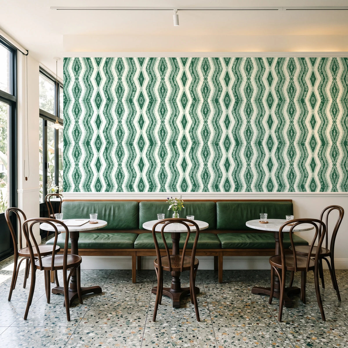 Gilded Rain Emerald geometric wallpaper above a green leather banquette in a sunlit neighborhood cafe