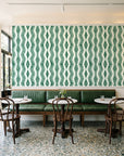 Gilded Rain Emerald geometric wallpaper above a green leather banquette in a sunlit neighborhood cafe