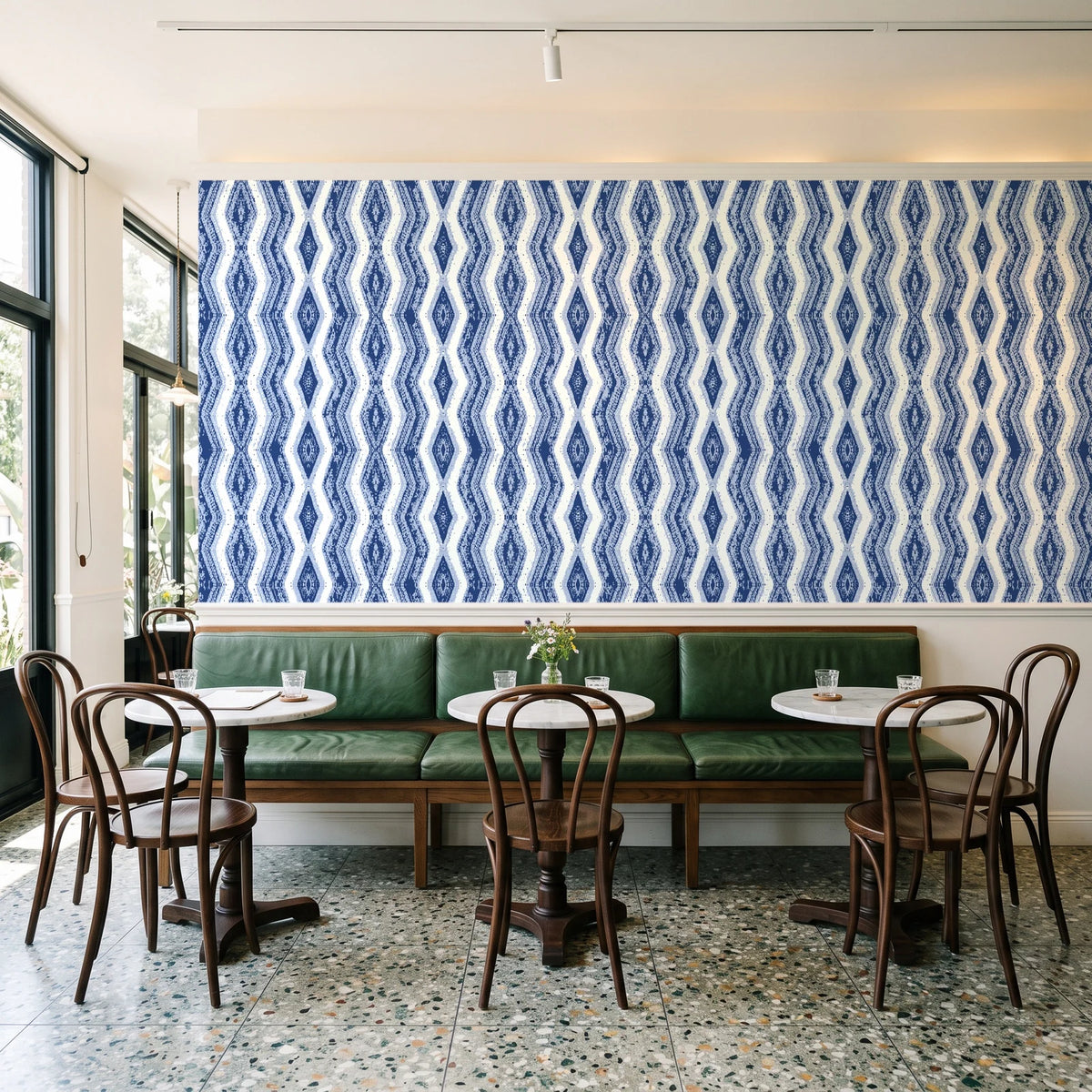 Gilded Rain Indigo geometric wallpaper above a green leather banquette in a sunlit neighborhood cafe