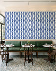 Gilded Rain Indigo geometric wallpaper above a green leather banquette in a sunlit neighborhood cafe