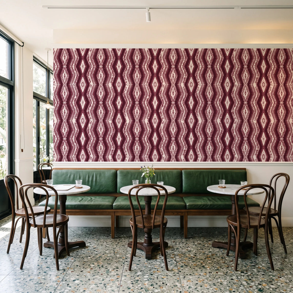 Gilded Rain Oxblood geometric wallpaper above a green leather banquette in a sunlit neighborhood cafe