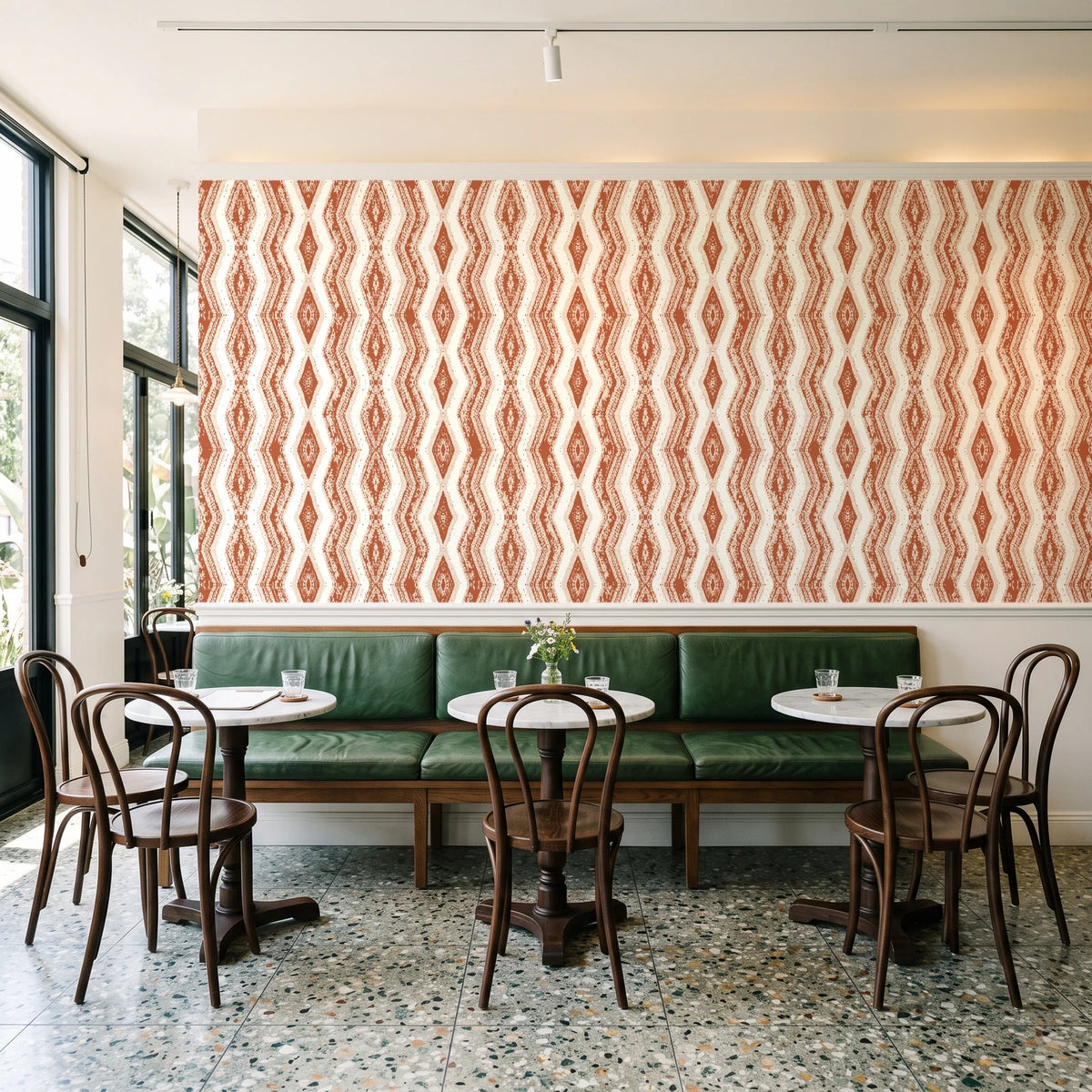 Gilded Rain Terracotta geometric wallpaper above a green leather banquette in a sunlit neighborhood cafe
