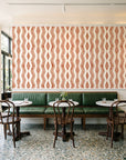 Gilded Rain Terracotta geometric wallpaper above a green leather banquette in a sunlit neighborhood cafe