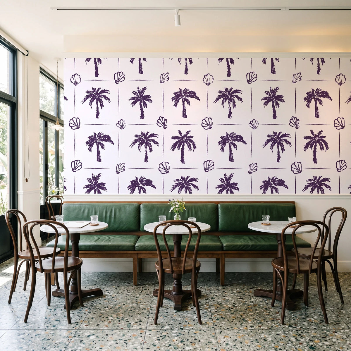 Ink & Shell Aubergine coastal palm and shell wallpaper above a green leather banquette in a sunlit neighborhood cafe