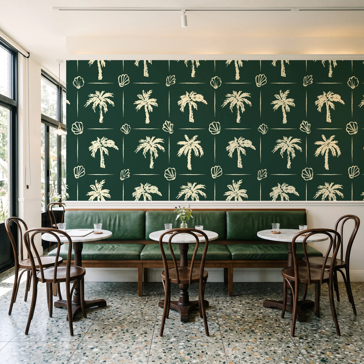Ink & Shell Forest coastal palm and shell wallpaper above a green leather banquette in a sunlit neighborhood cafe